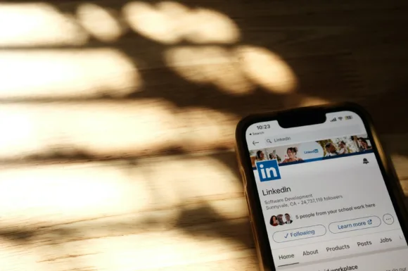 martphone su tavolo di legno che mostra un profilo aziendale su LinkedIn, con luce naturale che crea ombre e riferimento a funzionalità di LinkedIn Premium.
