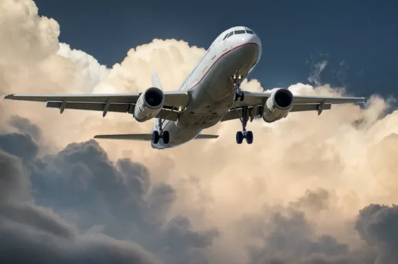 Aereo commerciale in volo con carrello di atterraggio esteso contro un cielo nuvoloso, illustrando la maestosità e la complessità del settore aeronautico.