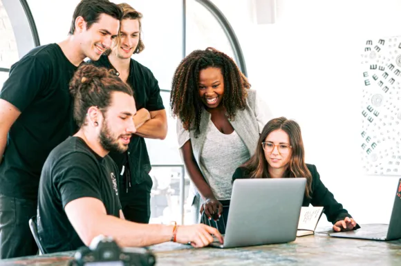 Team di giovani professionisti collabora attorno a un laptop in un ambiente di lavoro luminoso, riflettendo impegno e cooperazione nello studiare o lavorare su sistemi complessi come SAP.